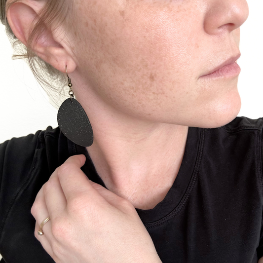 Close-up of a person wearing black ceramic earrings with a blurred background.