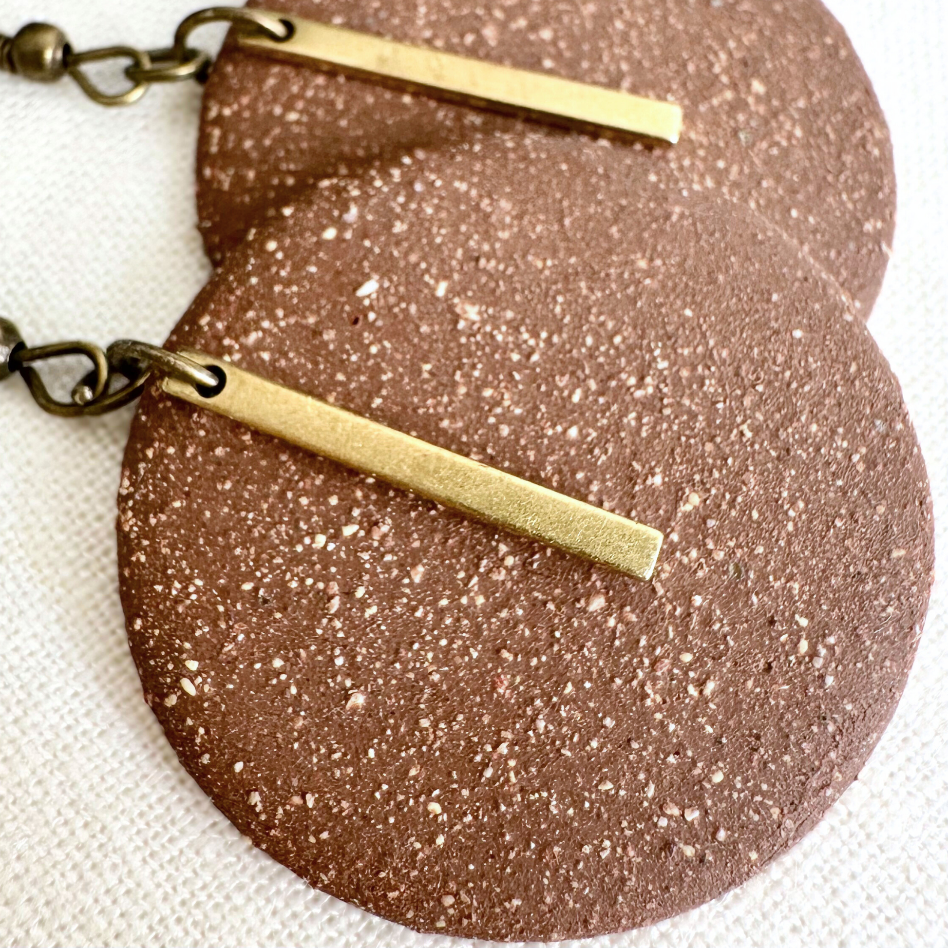Close up of the texture of brown handmade ceramic earrings with a gold charm.