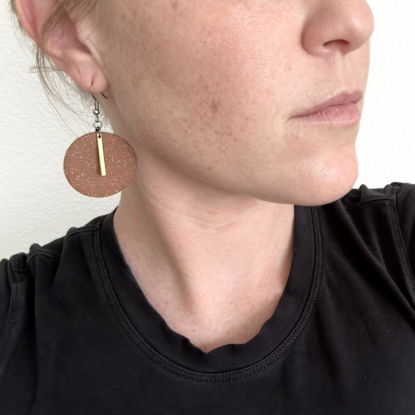 Close-up of a person wearing round red ceramic earrings with a gold charm.