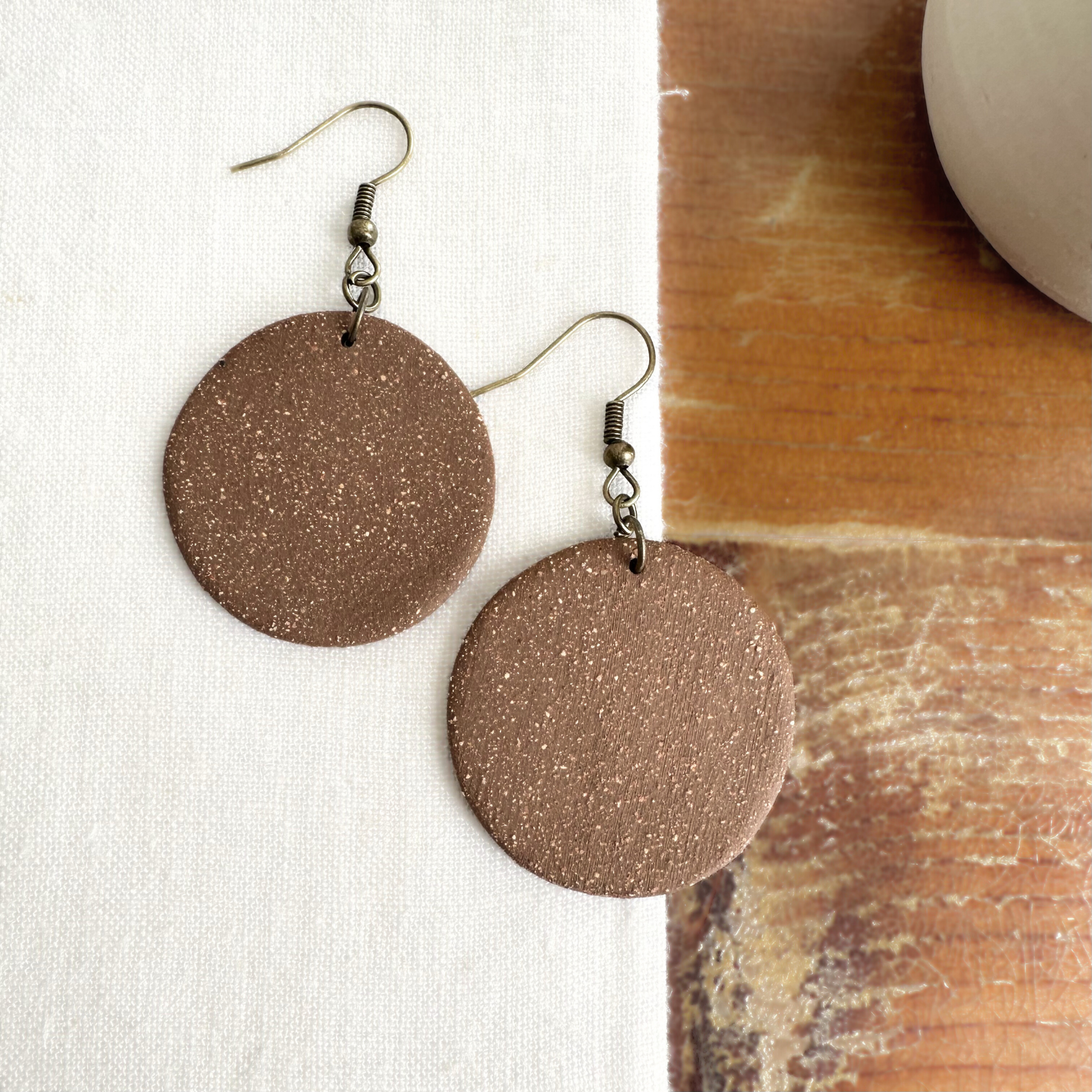 Pair of round brown handmade ceramic earrings on a partial white background with a wood accent.