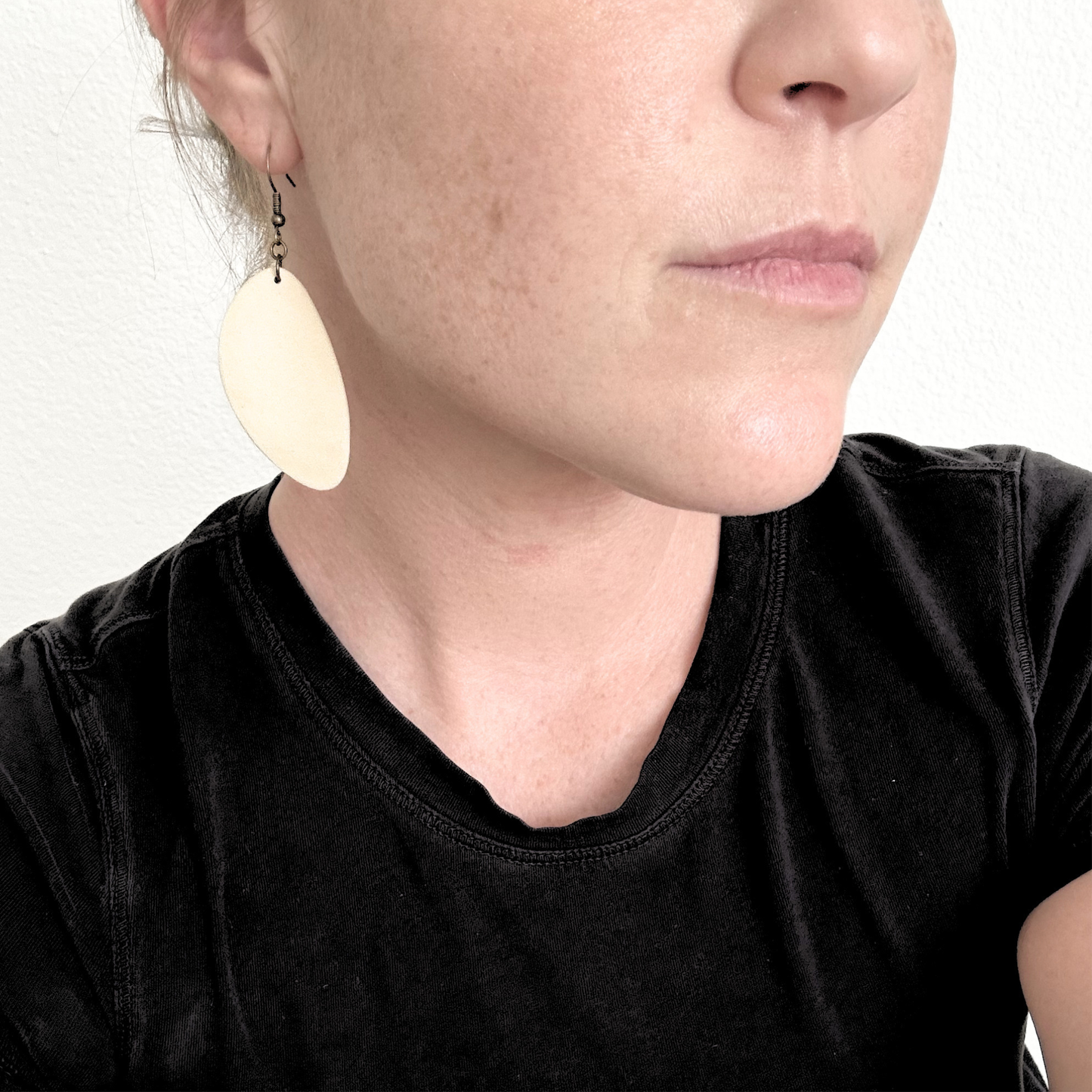 Close-up of a person wearing large white ceramic earrings with a plain background.