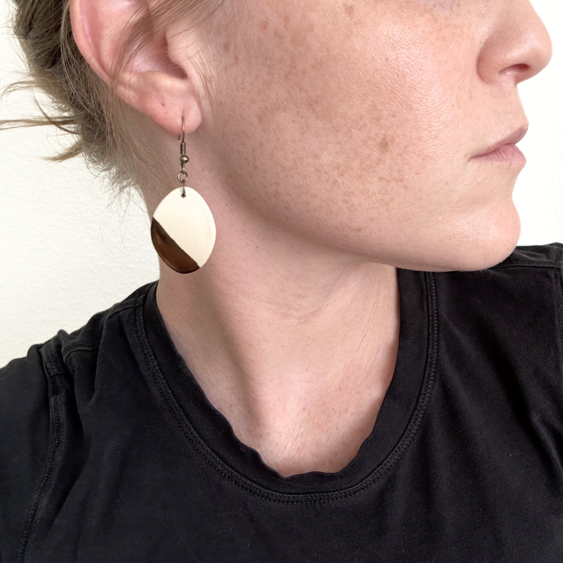 Close-up of a person wearing white ceramic gold dipped earrings with a black tee.