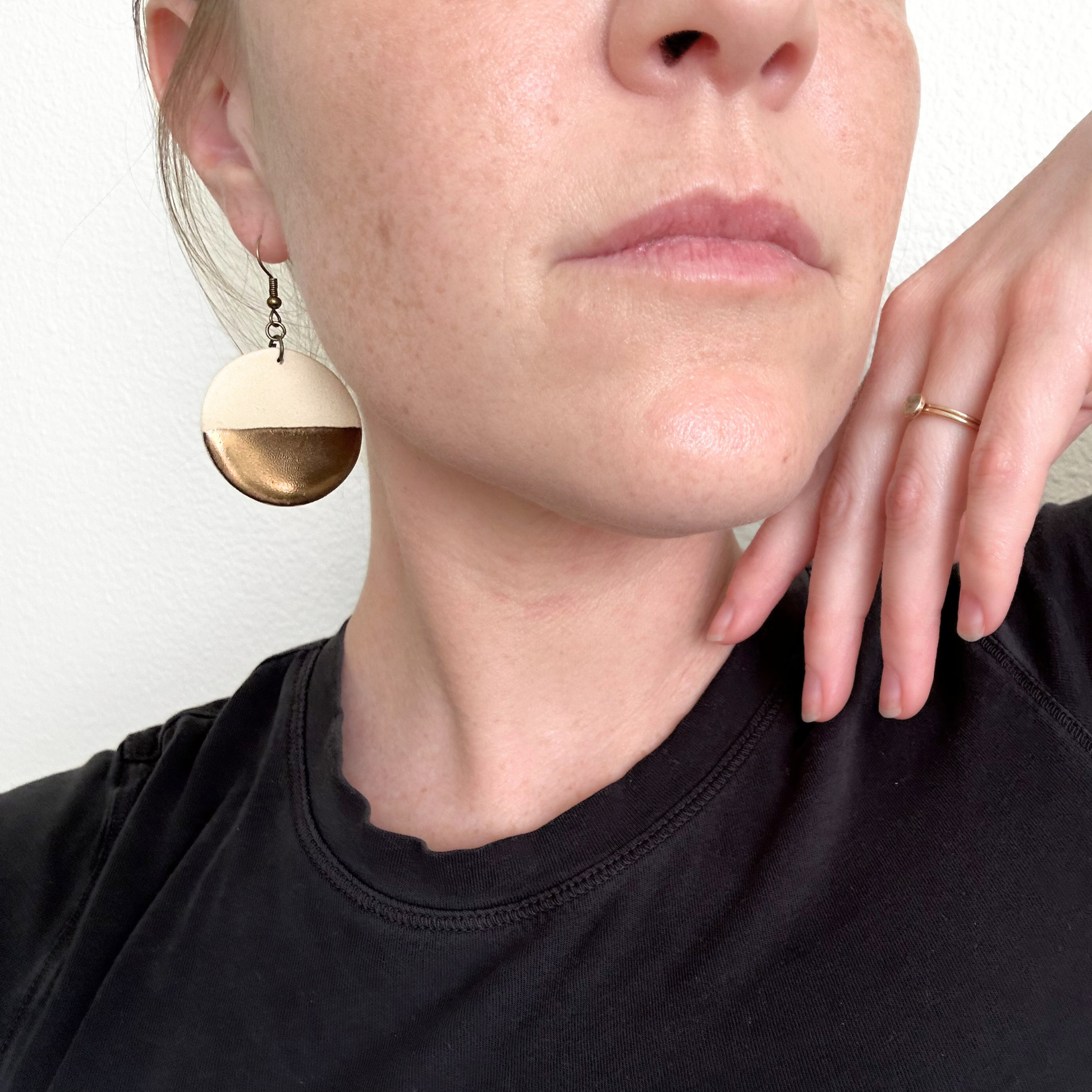 Close-up of a person wearing ceramic gold dipped earrings and a black top.